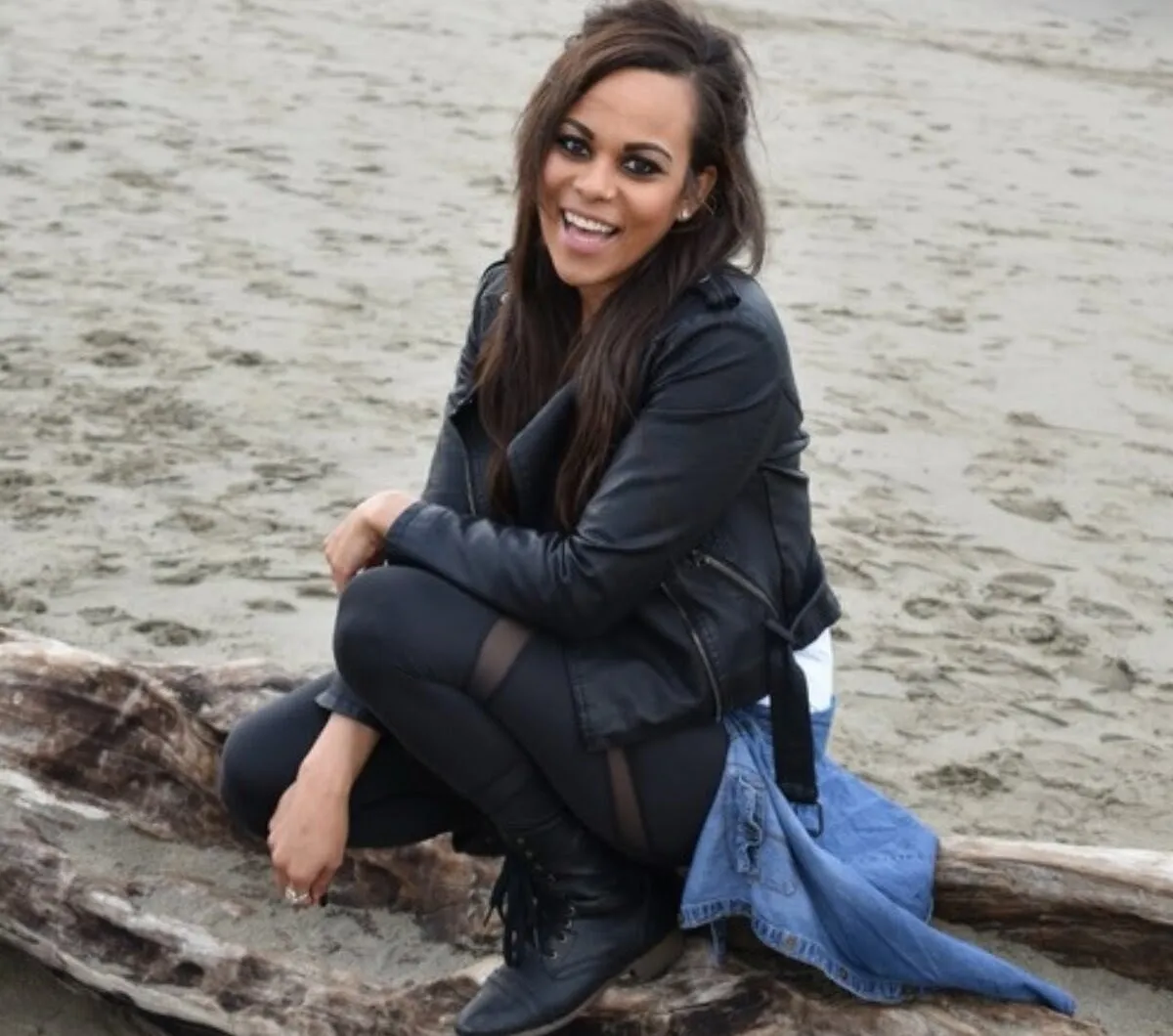 Kayla Mead smiling on a driftwood log at the beach